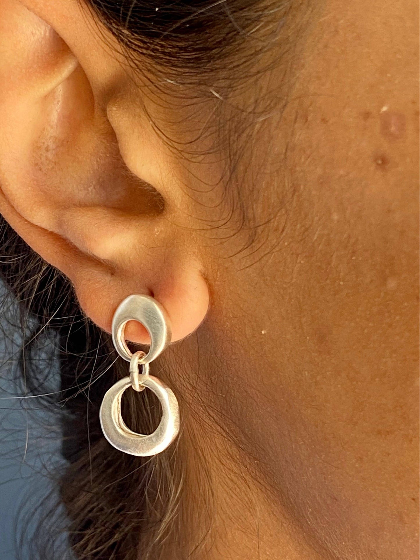 Silver circular drop earrings on ear, featuring two connected oval rings
