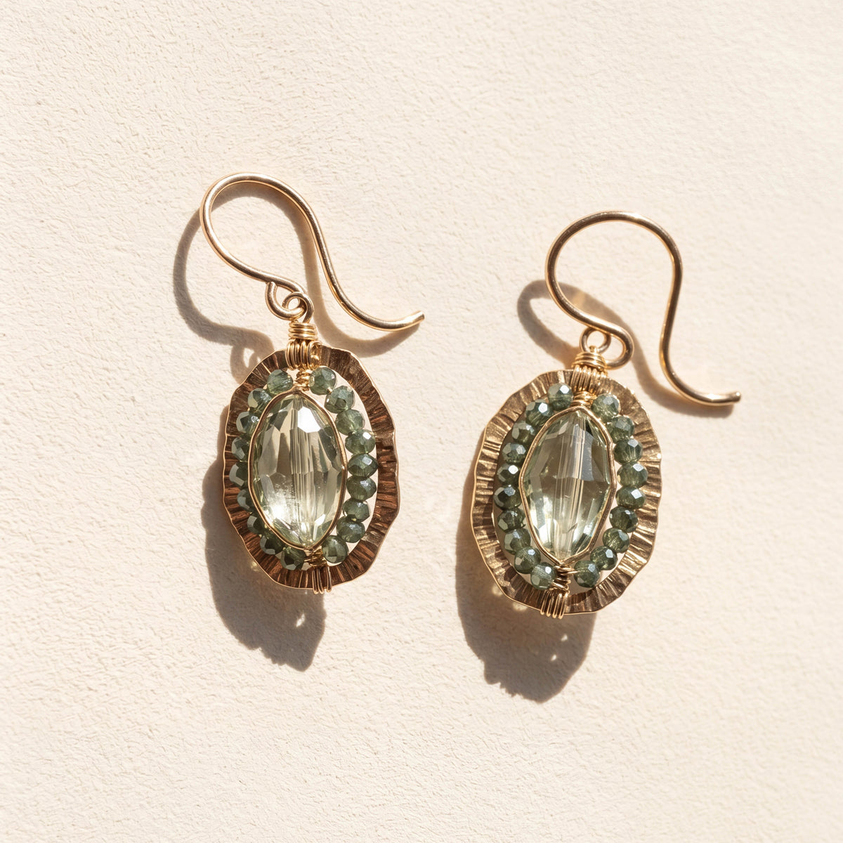 Gold-tone oval drop earrings with green faceted center stone and beaded halo.