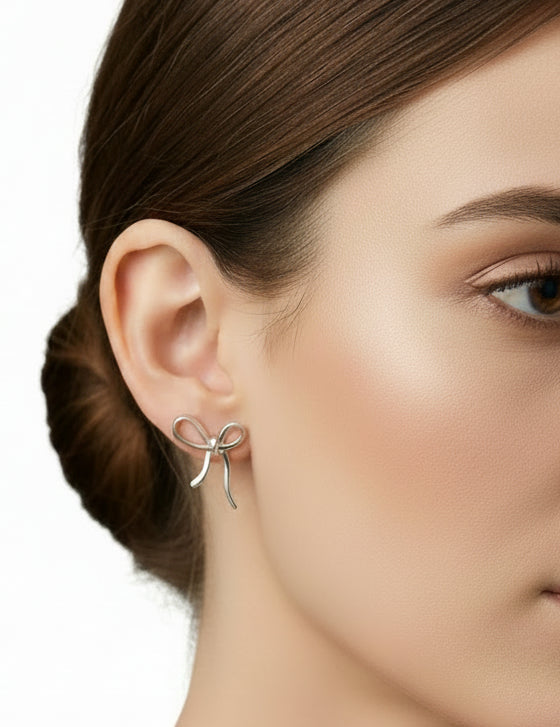 Ribbon bow stud earrings, silver-tone metal, shown on ear with dangling bow loops