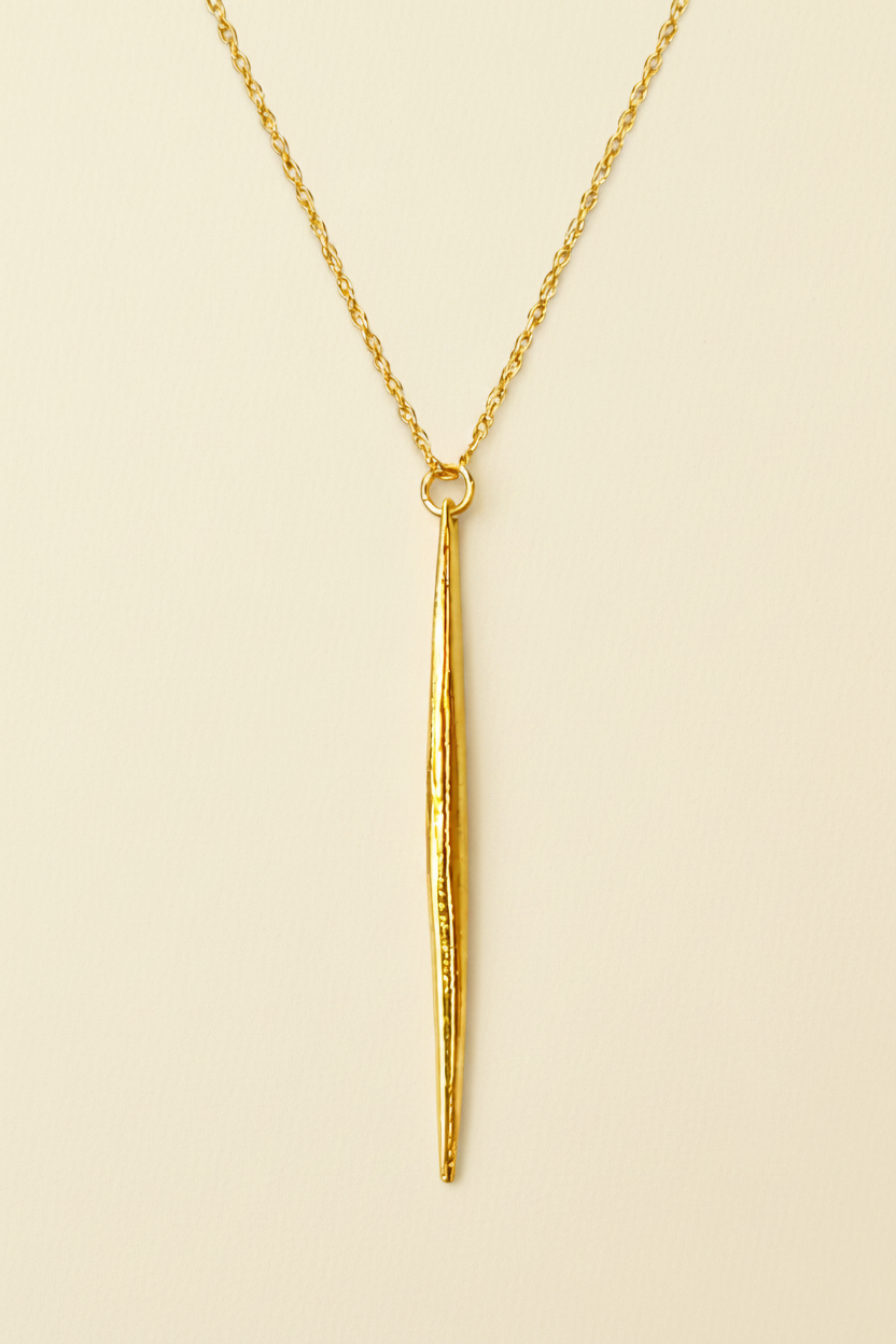Gold necklace with a long, thin pendant on a white background