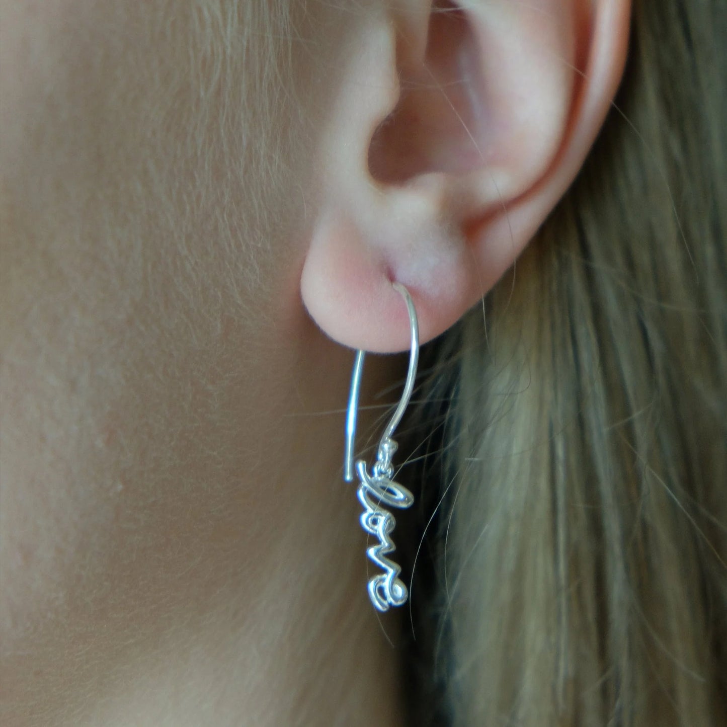 Silver script dangle earrings on ear with long curved hook and love charm