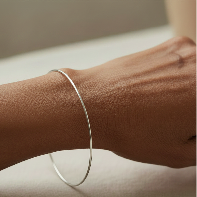 Thin silver bangle bracelet on wrist, smooth oval cuff
