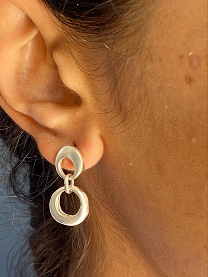 Silver circular drop earrings on ear, featuring two connected oval rings