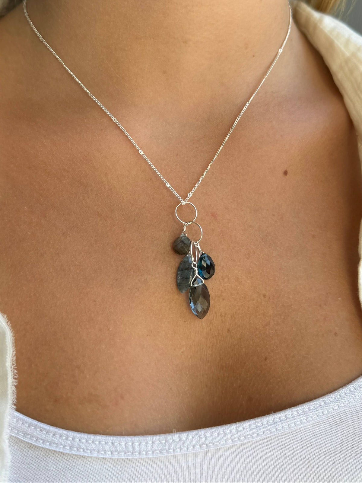 Silver chain necklace with linked rings and blue-green teardrop gemstone pendant