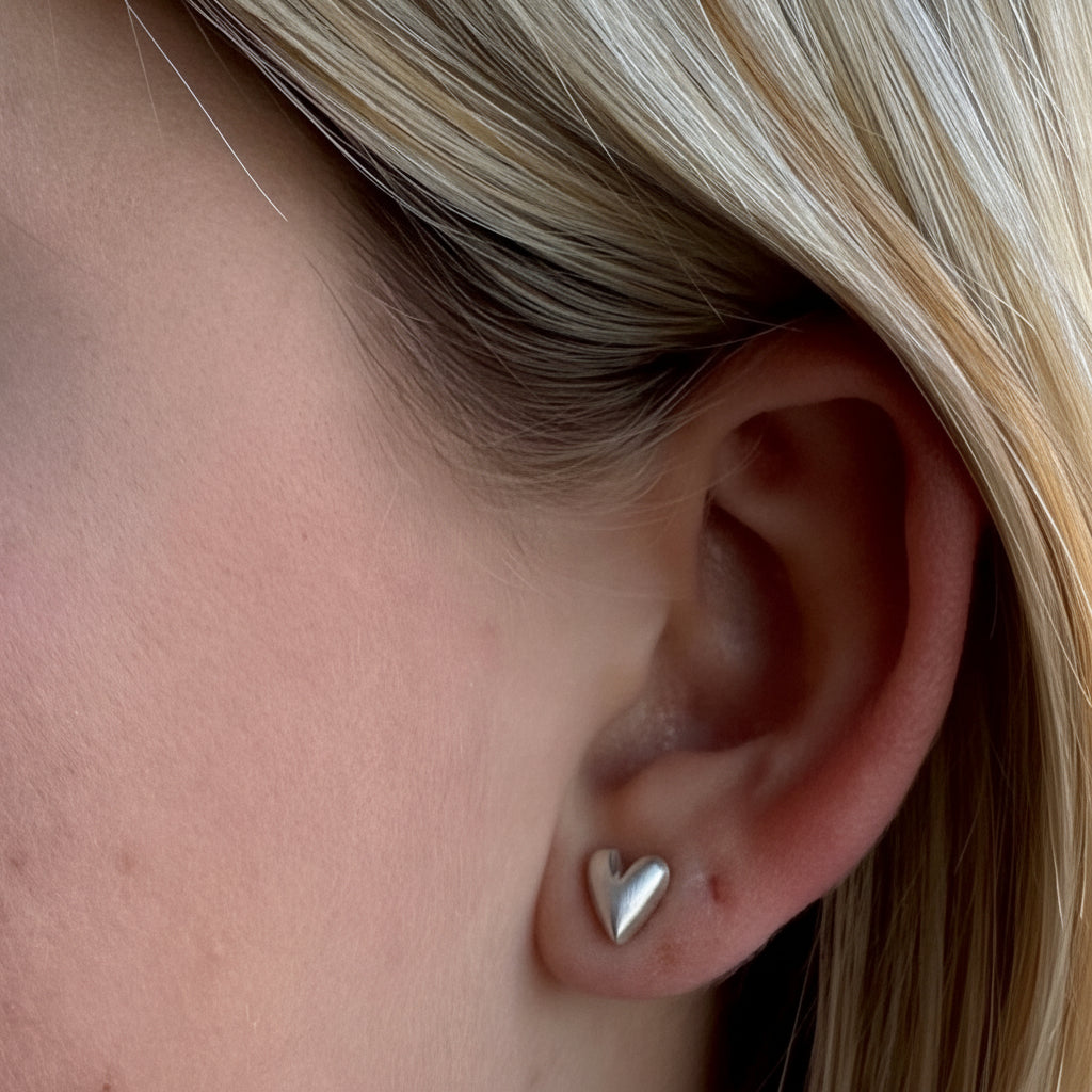Small puffy heart stud earrings, silver-tone, close-up on ear