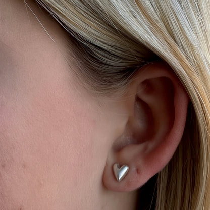 Small puffy heart stud earrings, silver-tone, close-up on ear