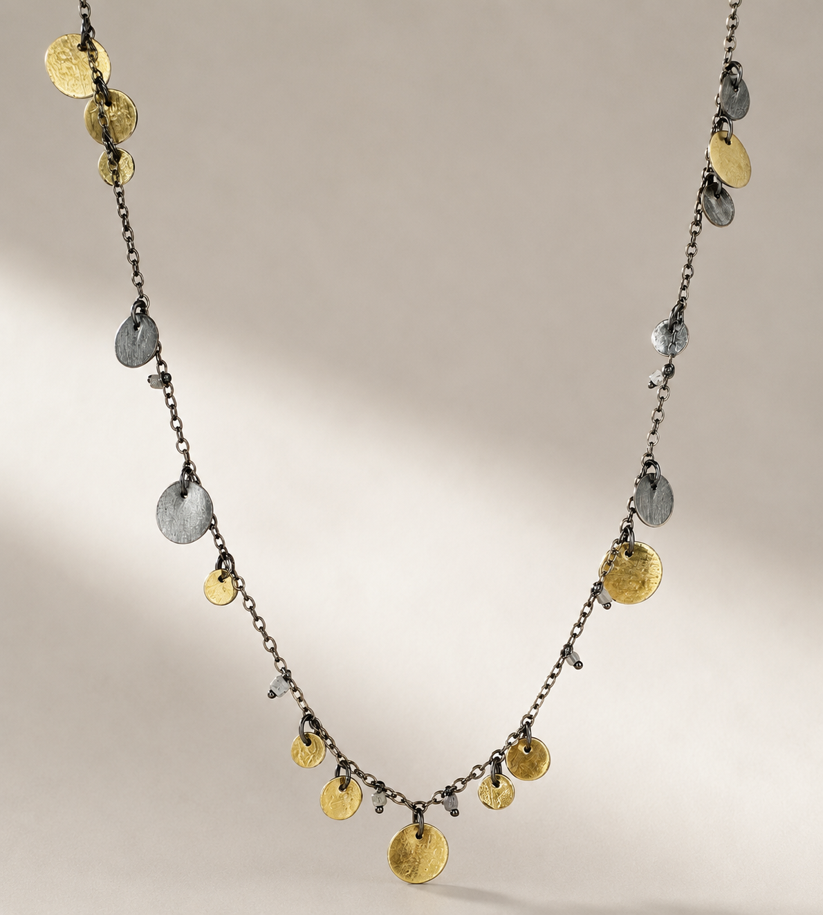 Coin disc charm necklace with alternating gold and silver medallions on a dark chain