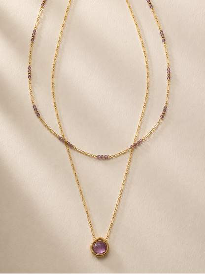 Gold layered necklace with purple bead accents and round purple pendant, long drape
