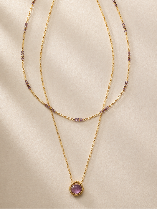 Gold layered necklace with purple bead accents and round purple pendant, long drape