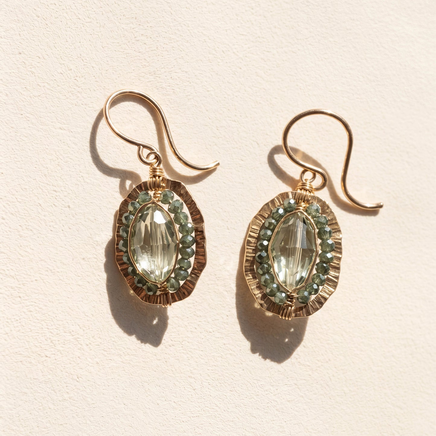 Gold-tone oval drop earrings with green faceted center stone and beaded halo.