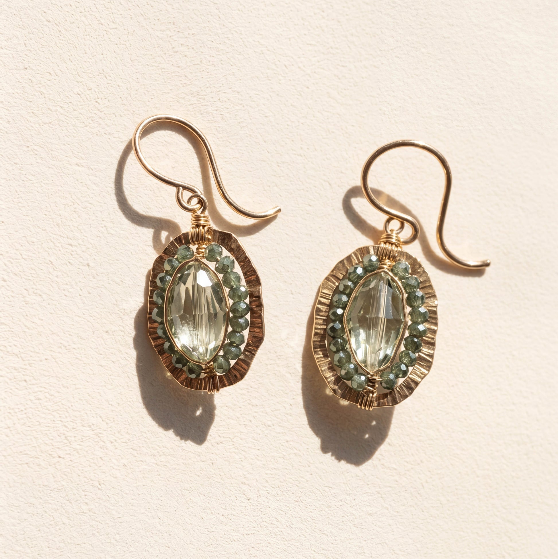 Gold-tone oval drop earrings with green faceted center stone and beaded halo.