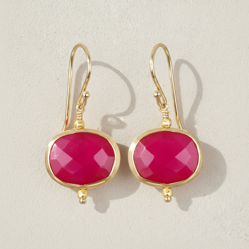 Gold earrings with pink gemstones on a beige background