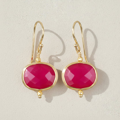 Gold earrings with pink gemstones on a beige background