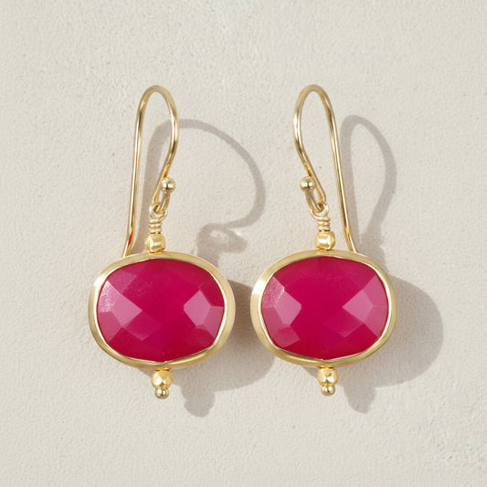 Gold earrings with pink gemstones on a beige background