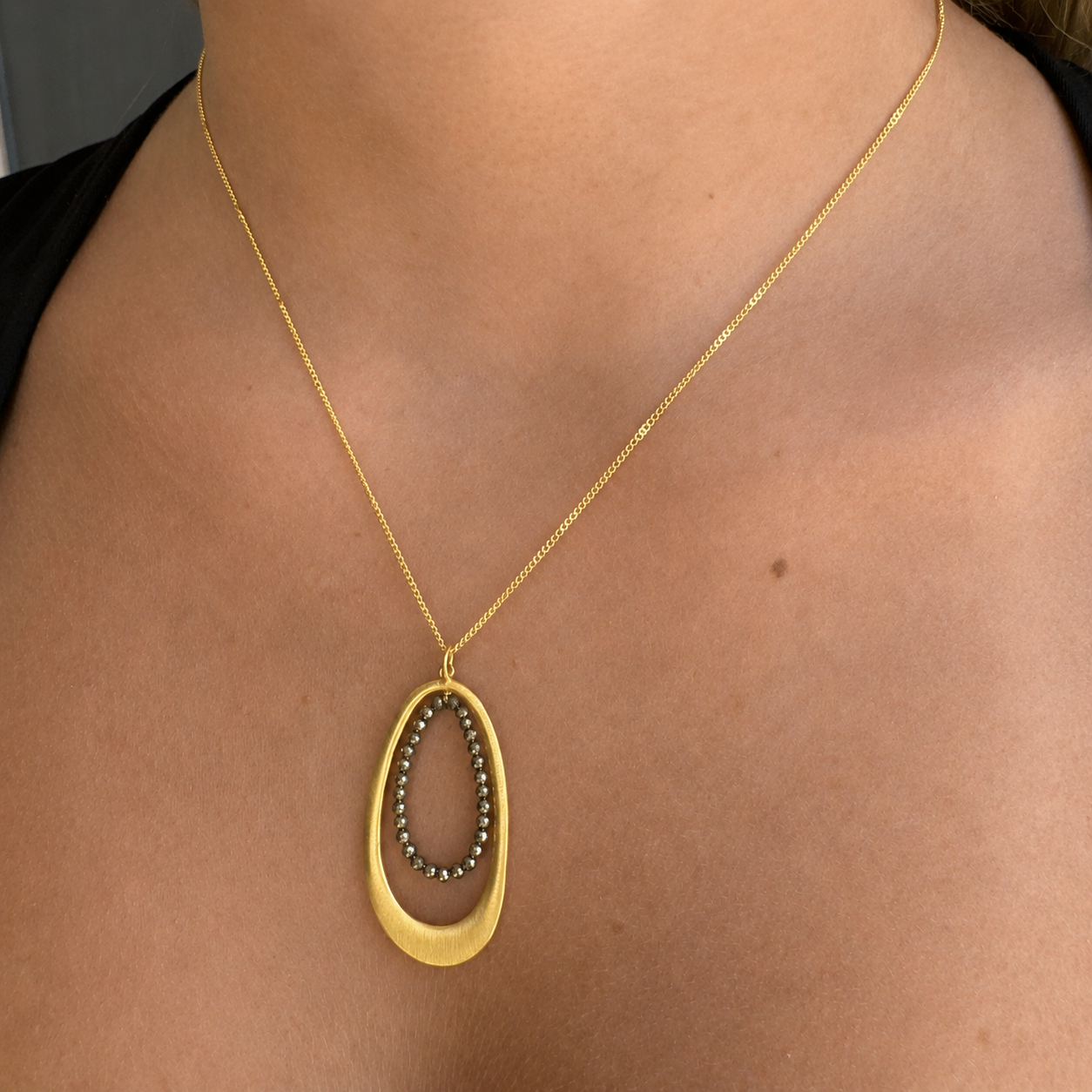 Oval pyrite-bead pendant necklace with gold chain and oval frame at neckline
