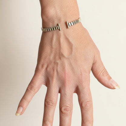 Striped silver cuff bracelet worn on wrist, with hinge bar closure and ridged band
