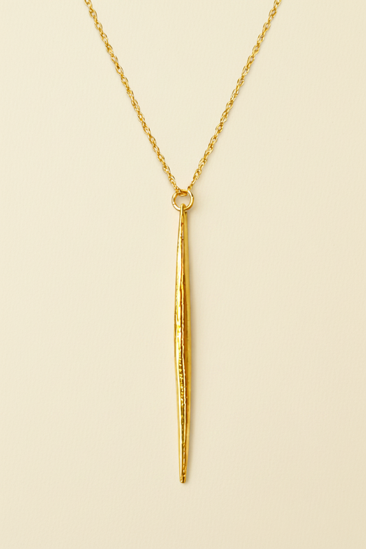 Gold necklace with a long, thin pendant on a white background