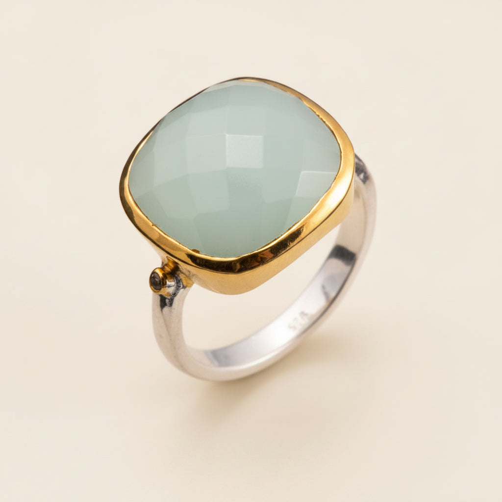 Ring with gold and silver band and light green stone on a white background
