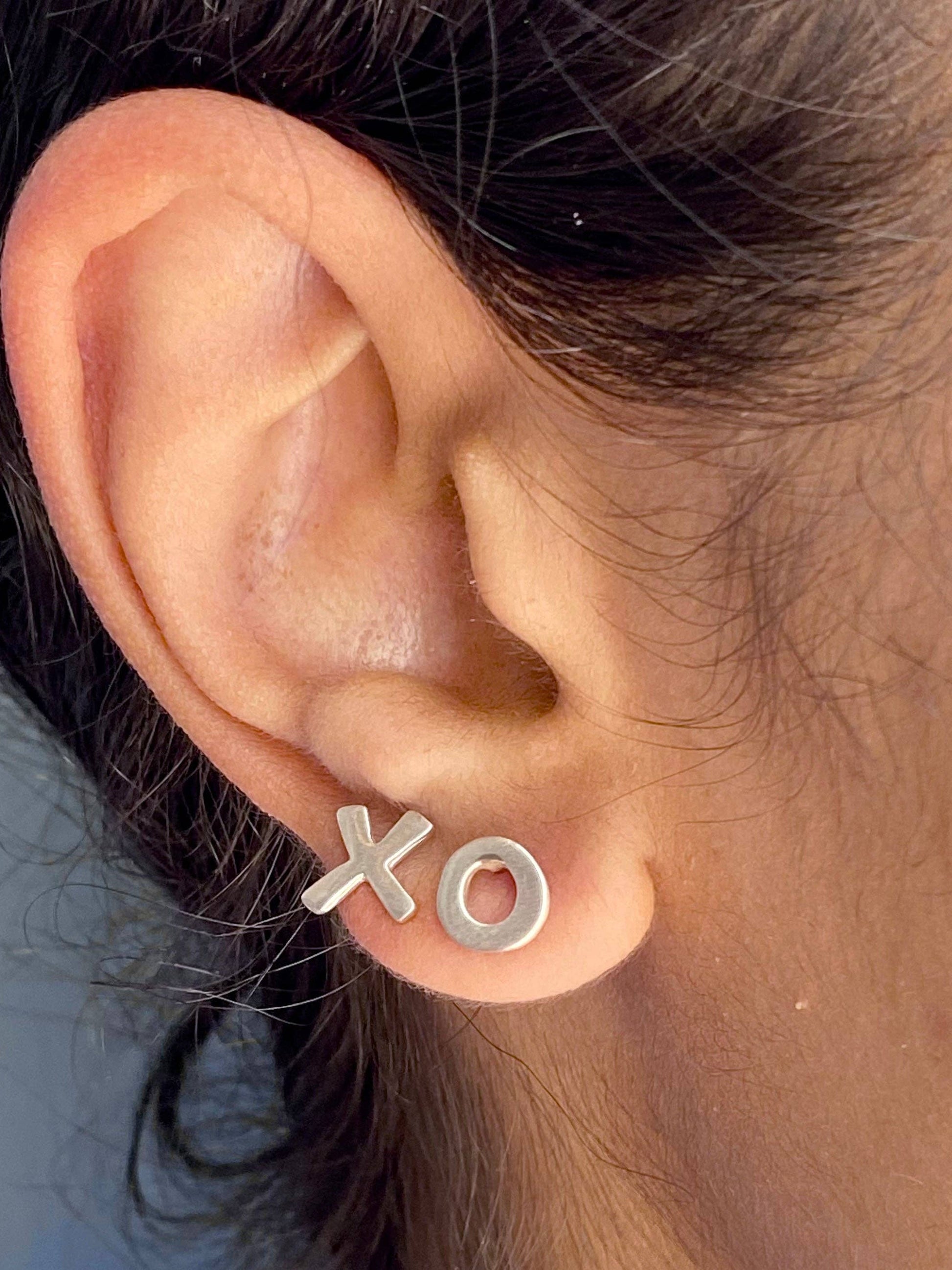 XO stud earrings on ear, X and O silver-tone letters with post backs