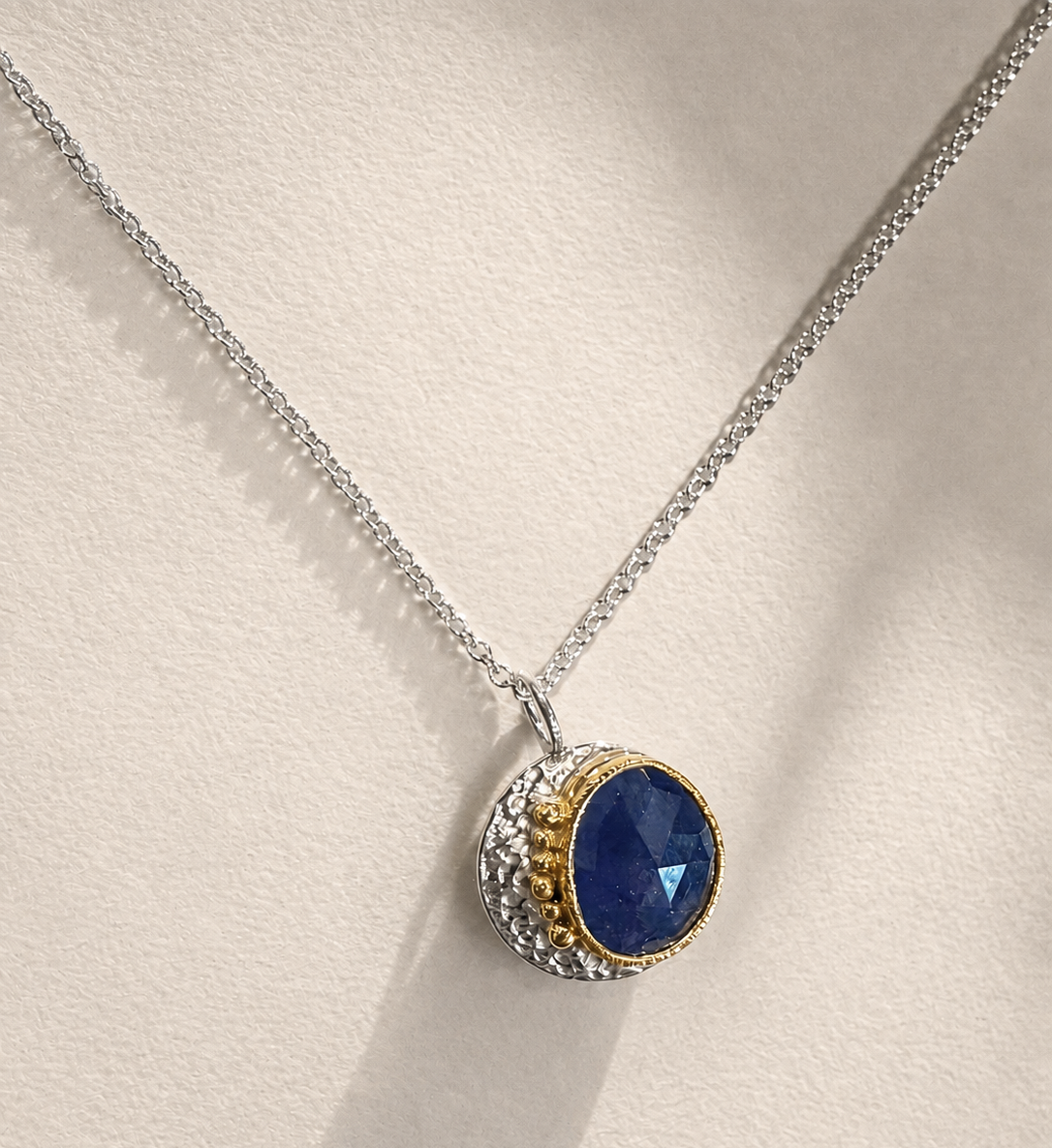 Round pendant necklace with dark blue sapphire-like stone and gold-tone halo on silver chain