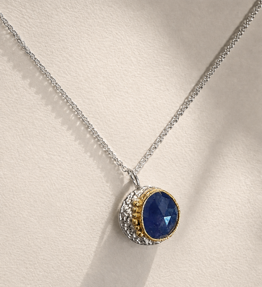 Round pendant necklace with dark blue sapphire-like stone and gold-tone halo on silver chain