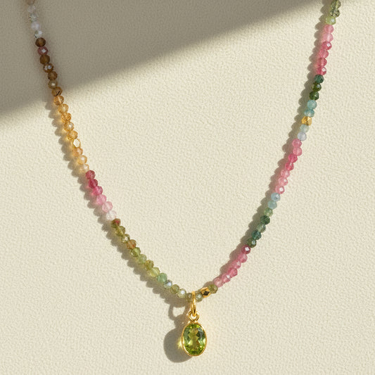 Multicolor beaded charm necklace with gold clasp and green teardrop pendant.