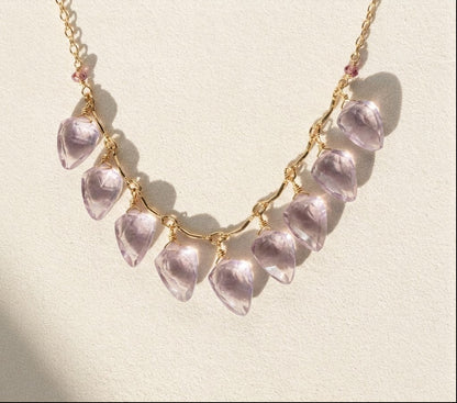 Gold-tone necklace with lilac petal-shaped charms in a curved row