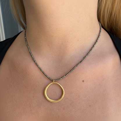 Gold open ring pendant necklace on dark beaded chain, styled at the neckline