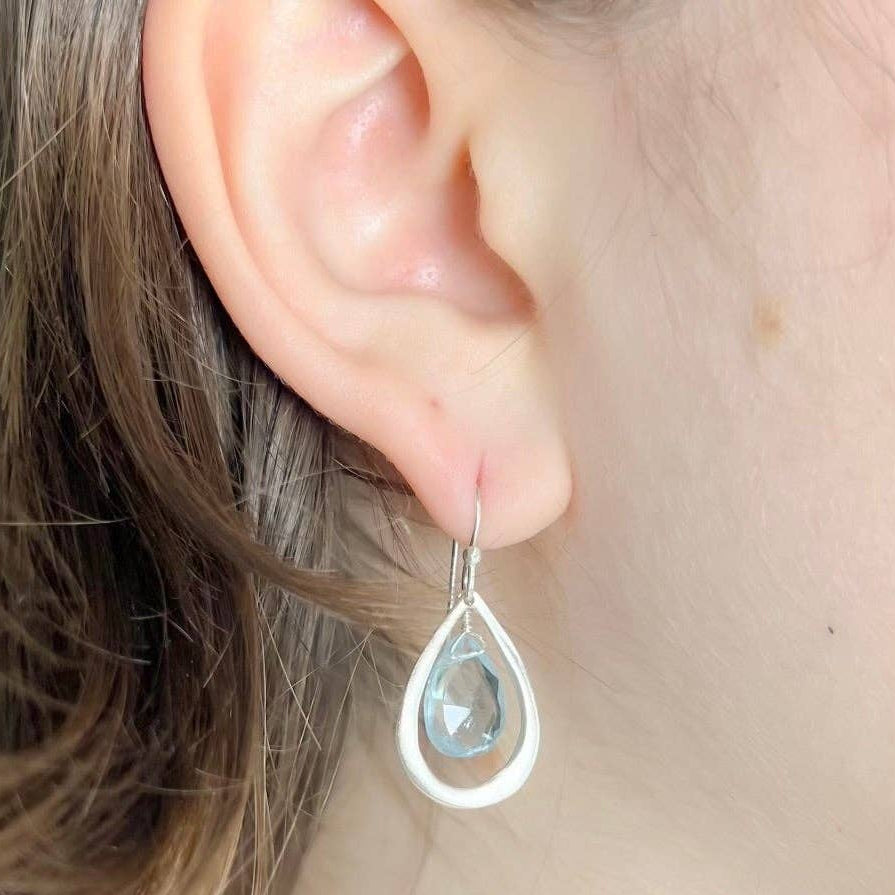 Teardrop gemstone earrings with blue Topaz stones and silver hooks, close-up.