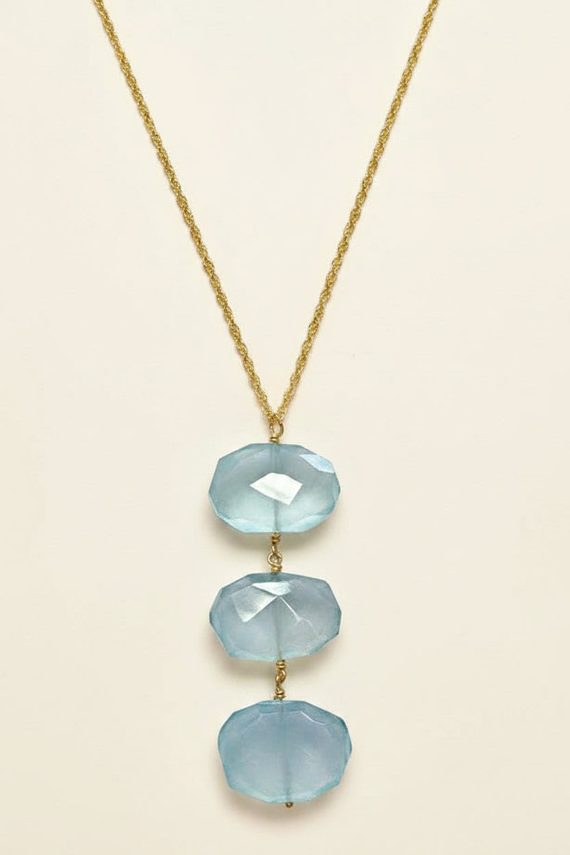 Necklace with three light blue faceted stones on a gold chain against a white background