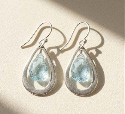 Pair of teardrop gemstone earrings with blue Topaz stones and silver hooks.