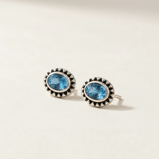 Gemstone stud earrings with blue oval center and silver beaded halo