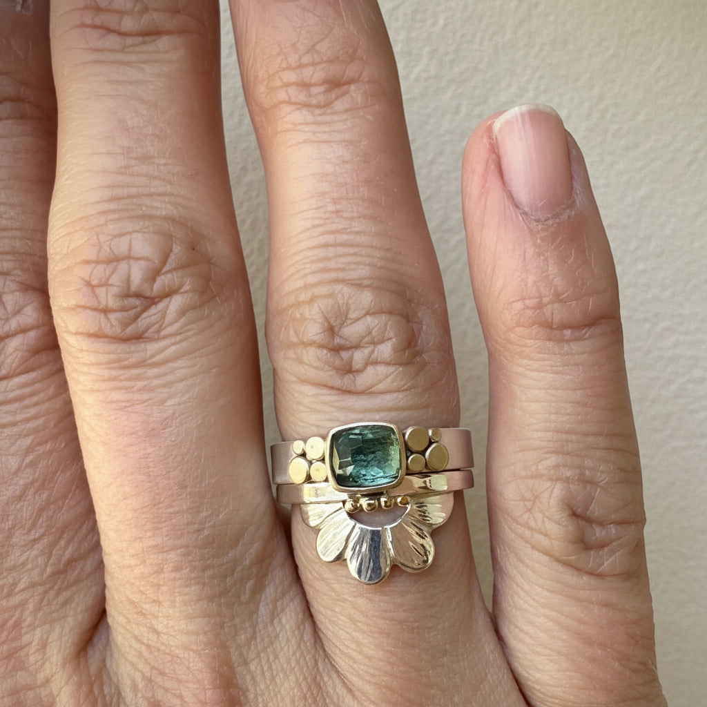 Gold ring with a green gemstone on a finger against a neutral background