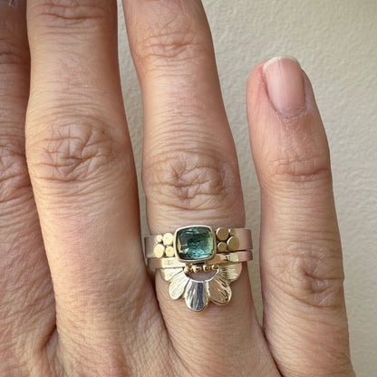 Gold ring with a green gemstone on a finger against a neutral background
