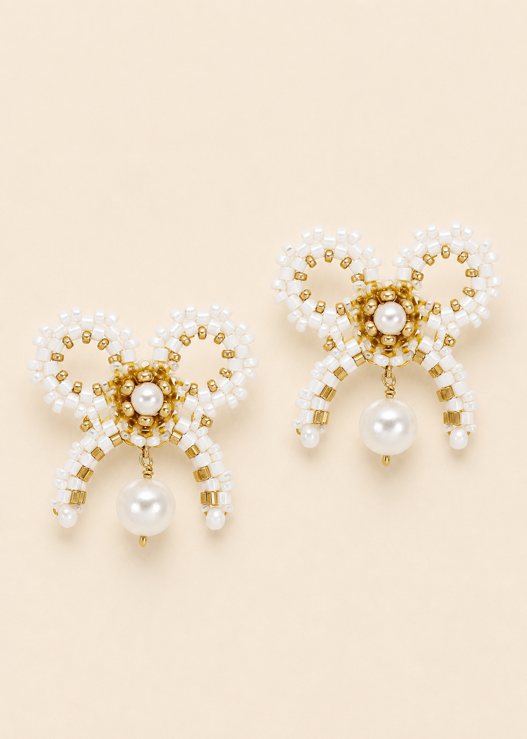 Pair of pearl and gold beaded earrings on a beige background
