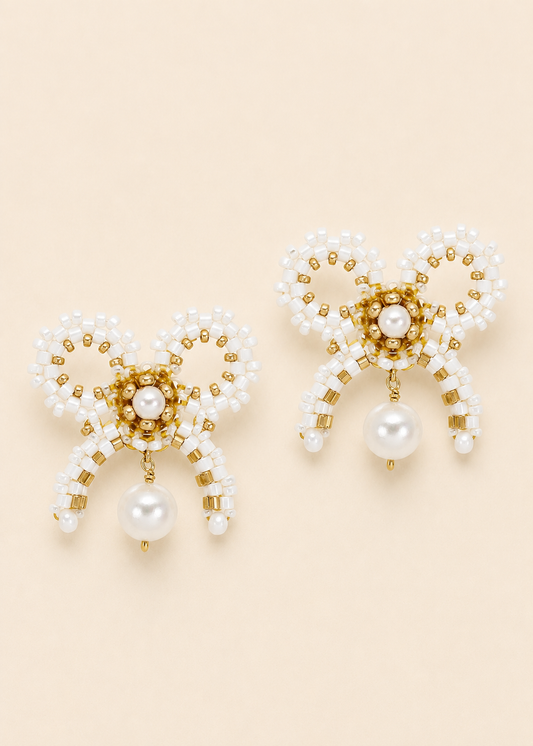 Pair of pearl and gold beaded earrings on a beige background