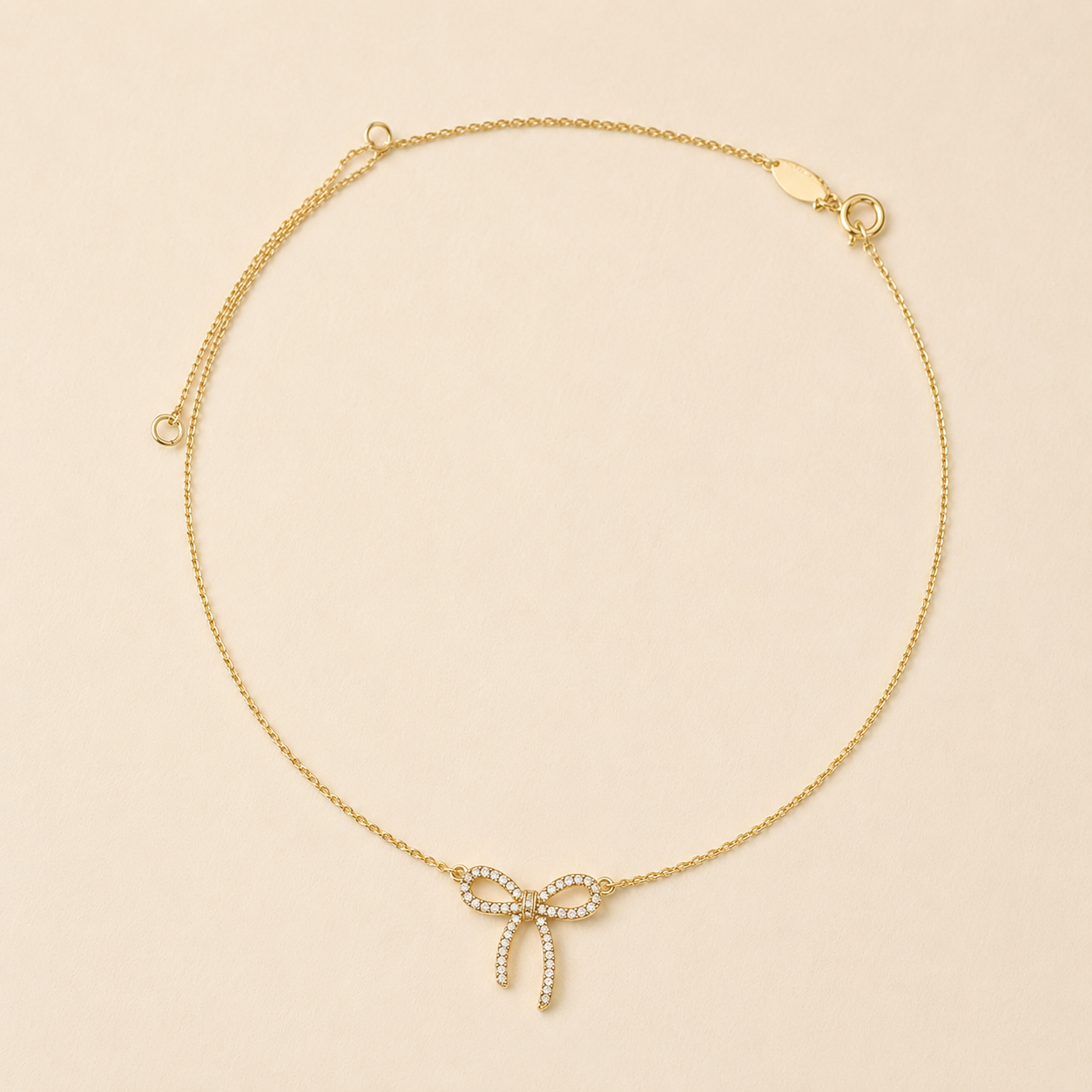 Gold-tone bow pendant necklace with small rhinestone accents and two dangling ribbon ends