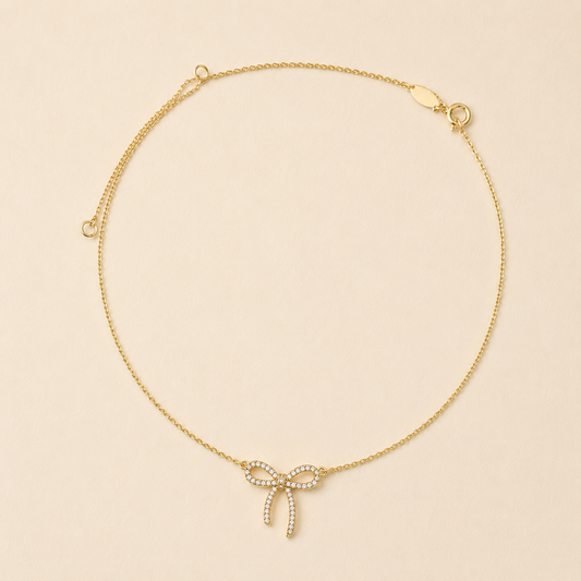 Gold-tone bow pendant necklace with small rhinestone accents and two dangling ribbon ends