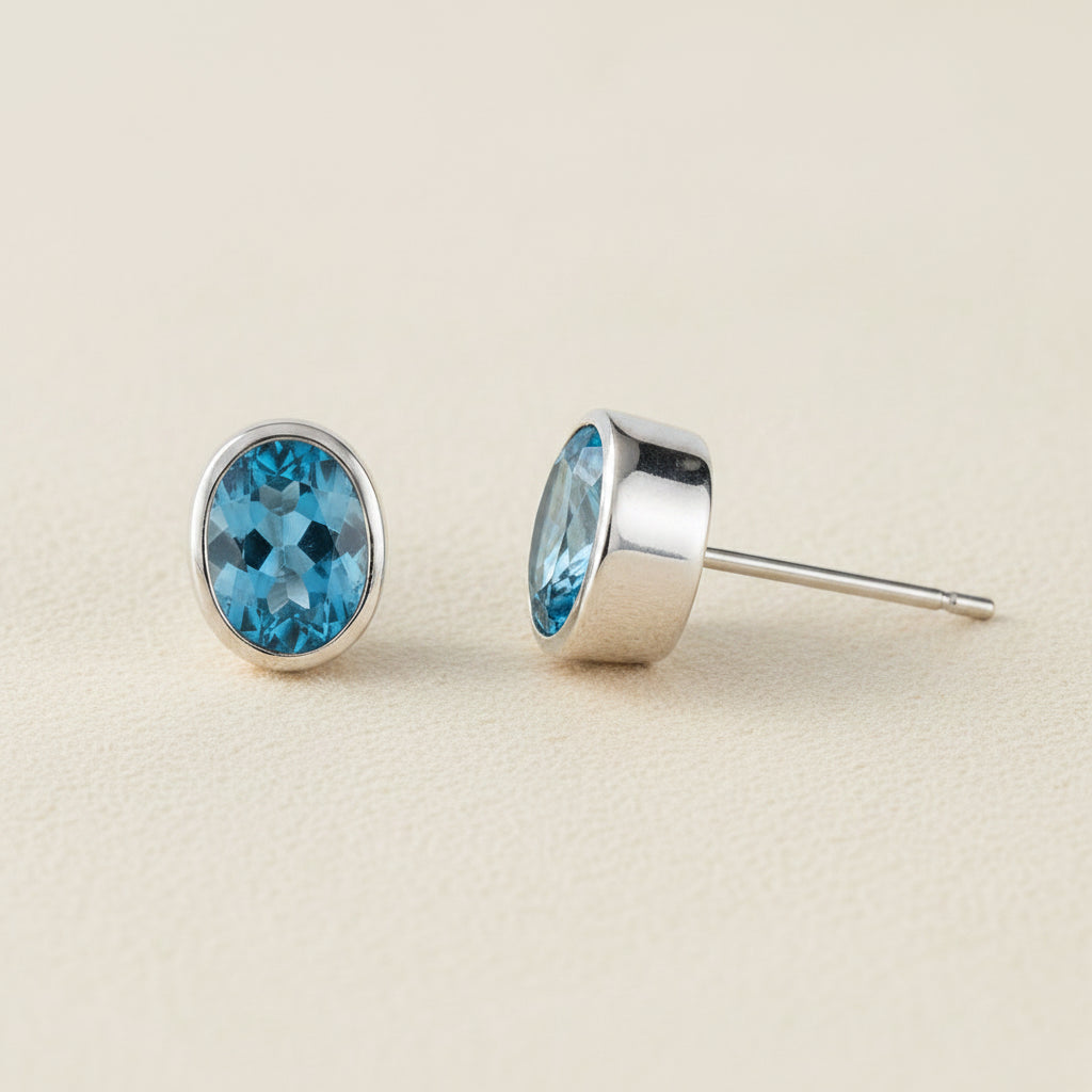 Oval blue gemstone stud earrings with silver bezel and post backing.