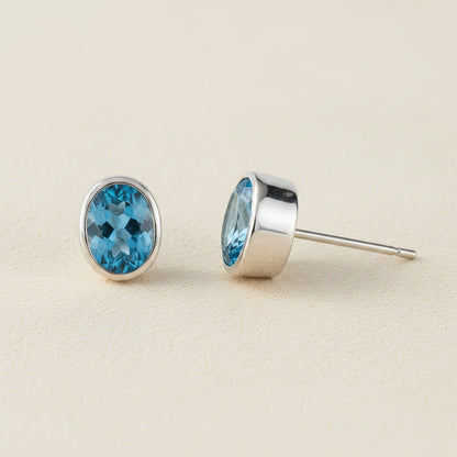 Oval blue gemstone stud earrings with silver bezel and post backing.