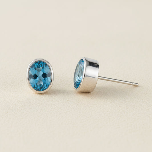 Oval blue gemstone stud earrings with silver bezel and post backing.