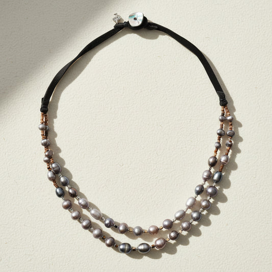 Double-strand pearl necklace with black cord on a white background