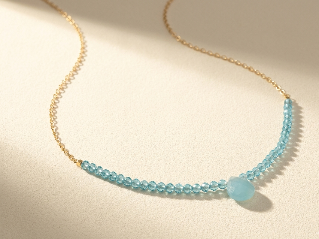 Beaded stones necklace with light blue faceted beads and small drop charm on gold chain