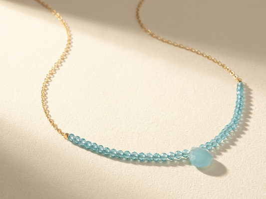 Beaded stones necklace with light blue faceted beads and small drop charm on gold chain