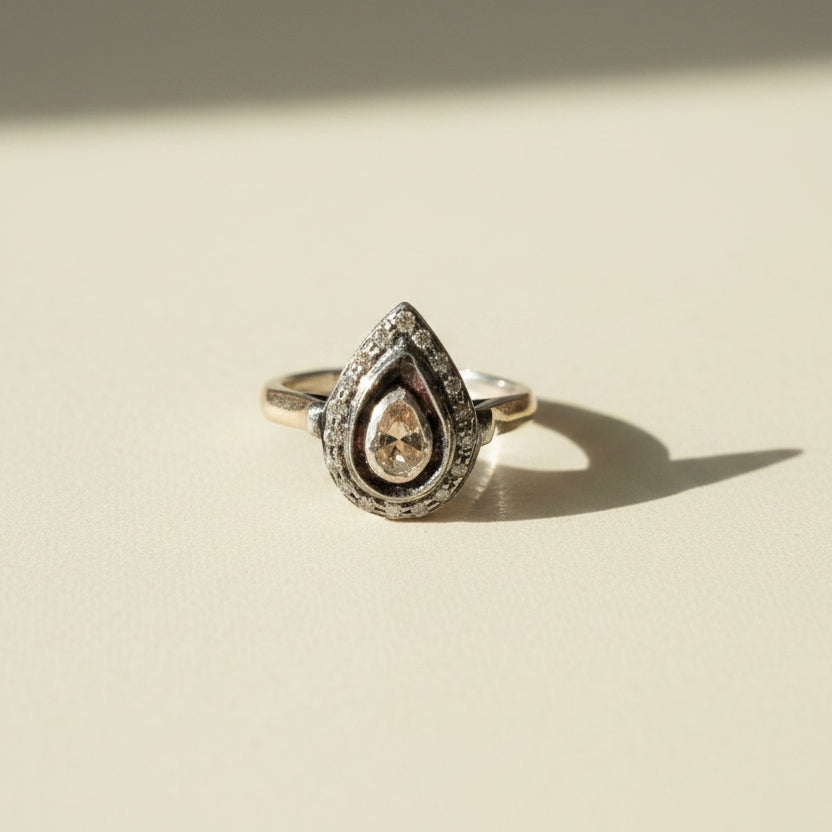 Two-tone teardrop diamond ring with pave border and teardrop center stone on gold band