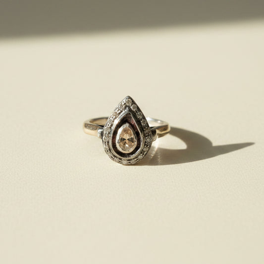 Two-tone teardrop diamond ring with pave border and teardrop center stone on gold band