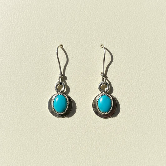 Turquoise oval earrings in round dark metal frames with dangling fishhook hooks
