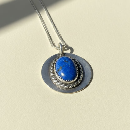 Silver-tone pendant necklace with blue oval gemstone set in braided rope bezel