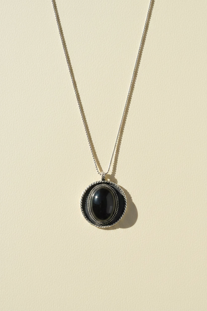 Shield pendant necklace with dark oval cabochon in textured round bezel
