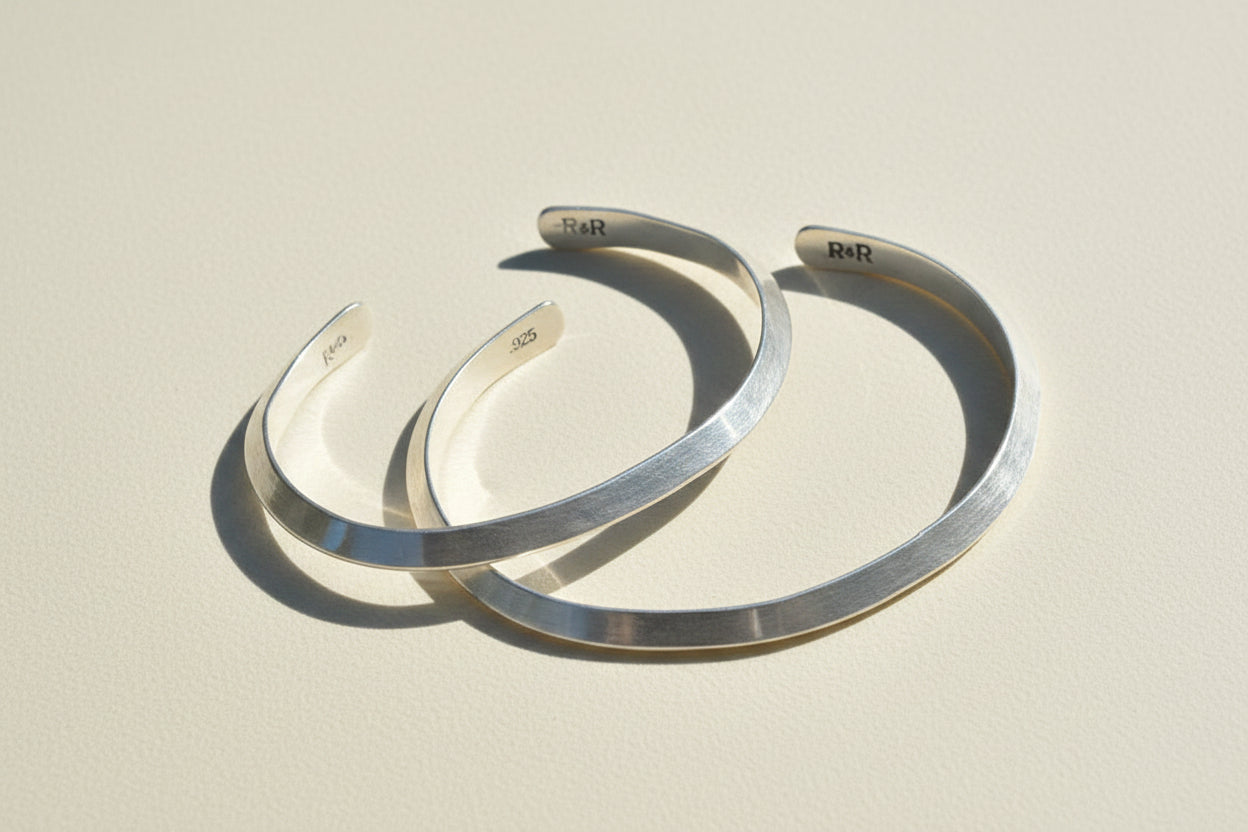 Pair of silver cuff bracelets, open V design with engraved inner logos